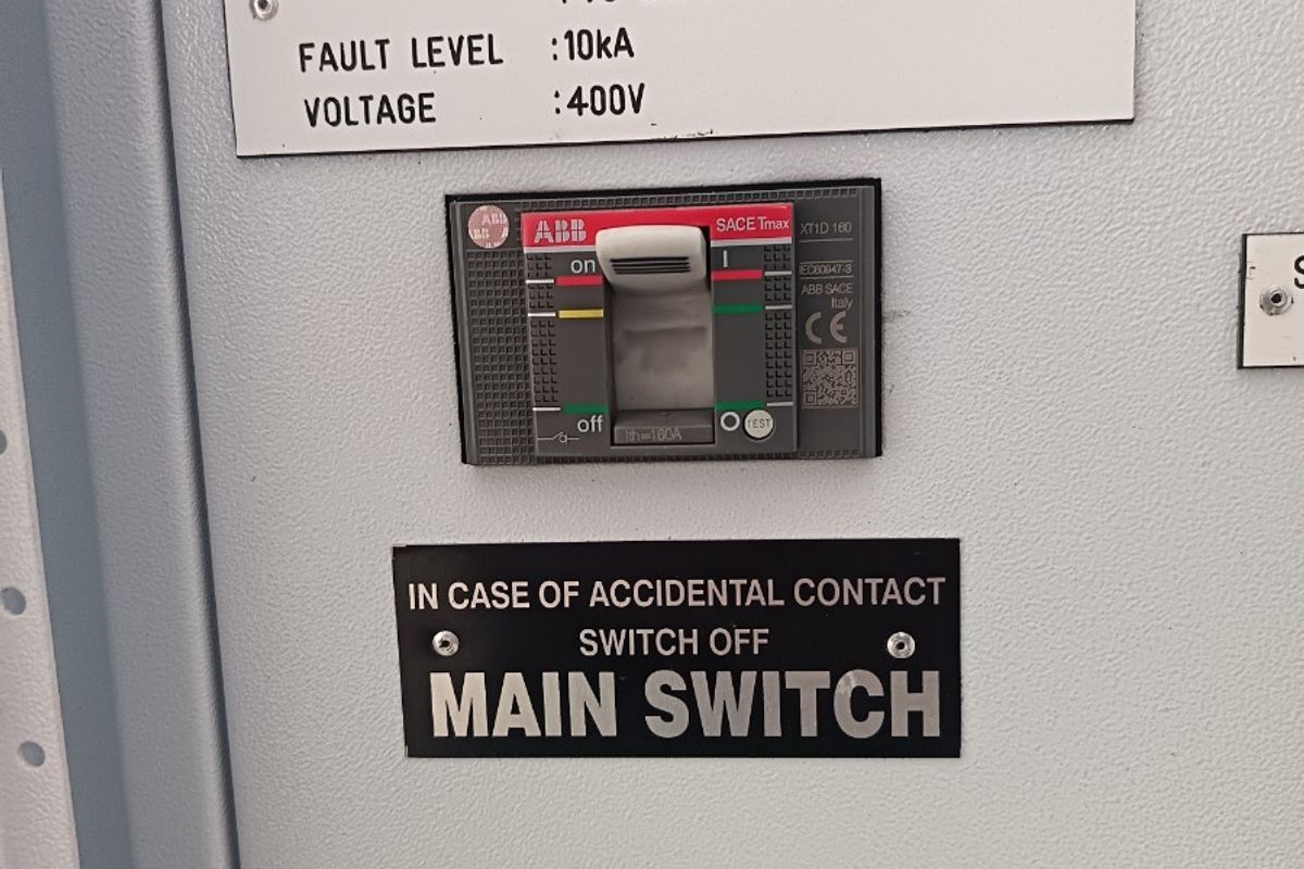 Close-up view of an industrial electrical distribution board featuring an ABB SACE Tmax circuit breaker and technical safety labeling.