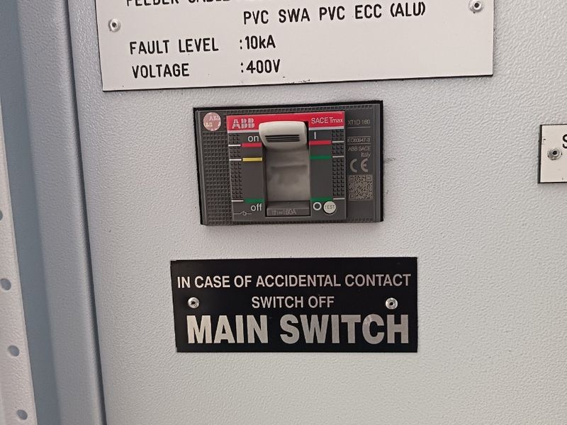 Close-up view of an industrial electrical distribution board featuring an ABB SACE Tmax circuit breaker and technical safety labeling.