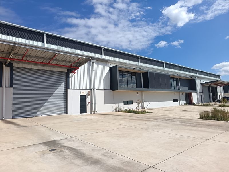 Modern industrial warehouse exterior featuring a large roller shutter door, concrete hardstand, and contemporary metal cladding with integrated fire safety systems.