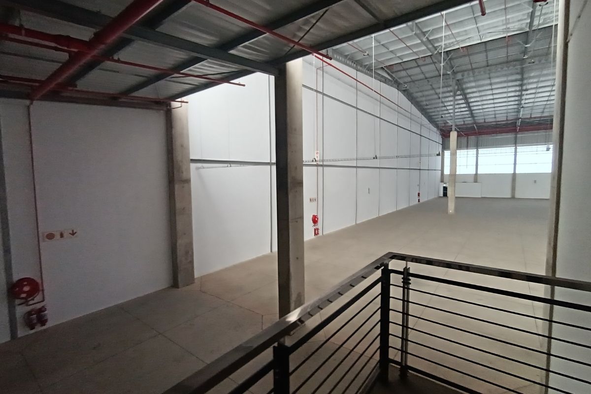 Spacious industrial warehouse interior featuring high ceilings, exposed fire suppression systems, concrete flooring, and structural columns with a mezzanine viewing area.