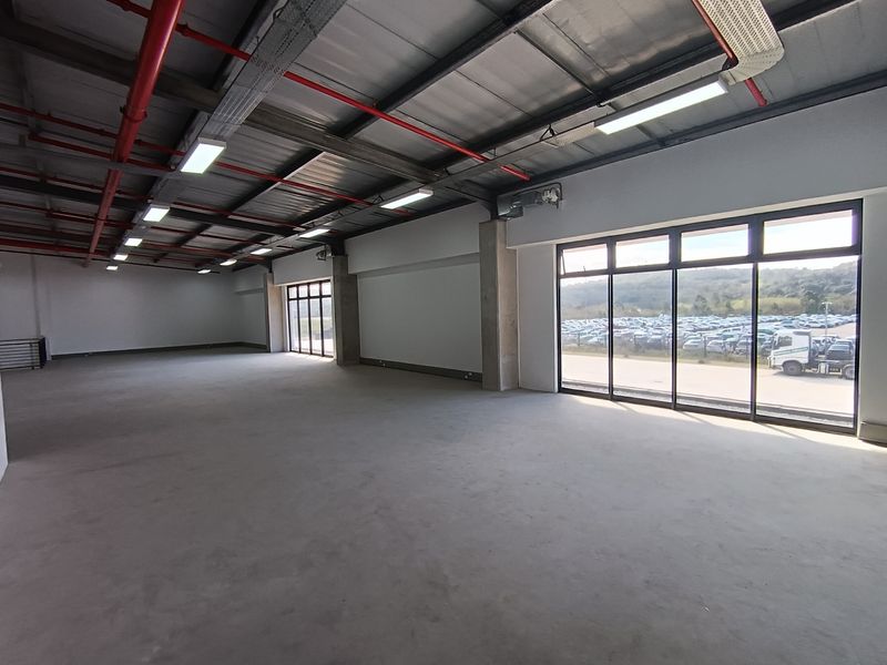 Spacious industrial utility area featuring high ceilings with exposed infrastructure, concrete flooring, and large windows providing ample natural light.