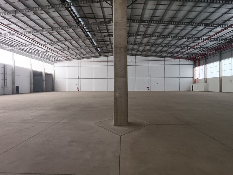 A spacious, empty industrial warehouse featuring high ceilings with exposed steel trusses, polished concrete flooring, and large windows providing ample natural light.