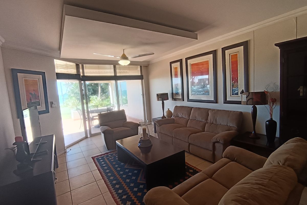A comfortable living room featuring tiled flooring, a recessed ceiling with a fan, and large sliding glass doors providing access to the patio.