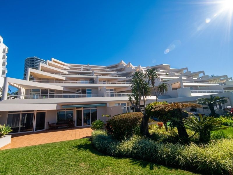 A view of the rear elevation of a multi-story apartment complex featuring tiered balconies, sliding glass doors, and a well-maintained landscaped garden area.