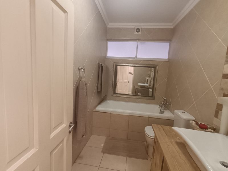 A functional bathroom featuring a built-in bathtub, toilet, and a vanity with a basin, finished with neutral wall and floor tiles.