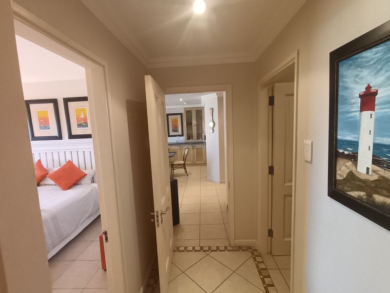 A bright hallway featuring tiled flooring and coved ceilings, providing access to the bedroom and kitchen areas of the apartment.
