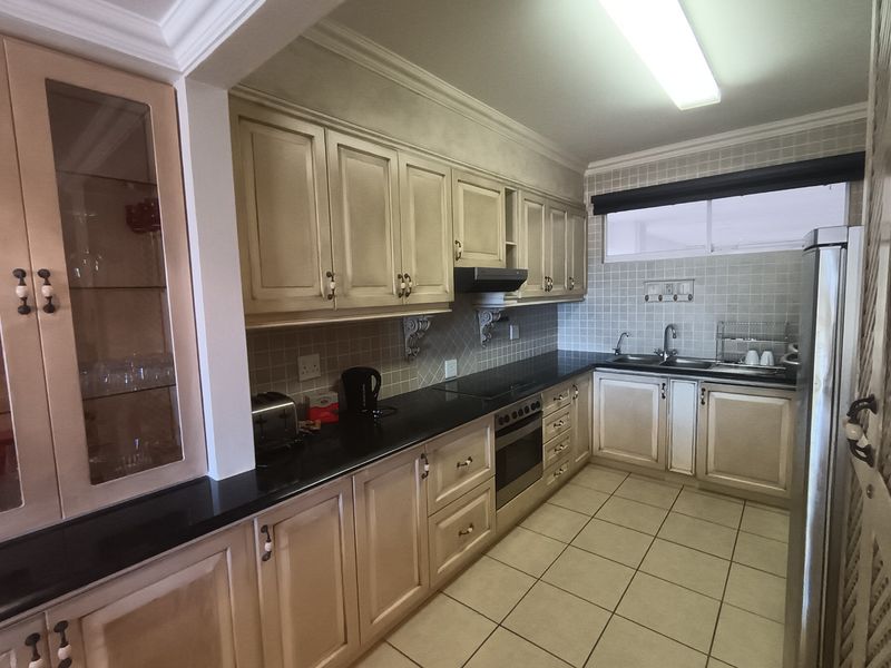 A functional kitchen featuring classic cabinetry, granite countertops, a double basin sink, built-in oven, and tiled finishes throughout.