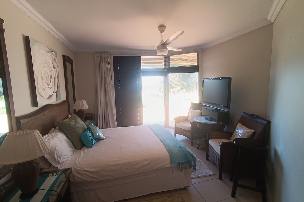 A comfortable bedroom featuring tiled flooring, a ceiling fan, and large sliding glass doors that provide natural light and access to the outdoors.