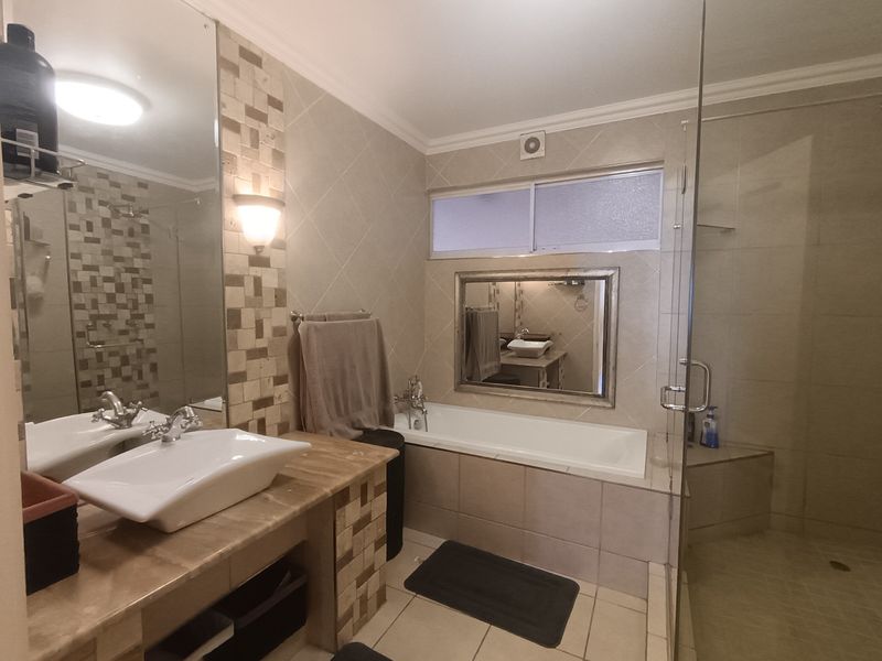 A well-appointed bathroom featuring a stone-topped vanity with a vessel sink, a built-in bathtub, and a separate glass-enclosed shower with decorative tile accents.