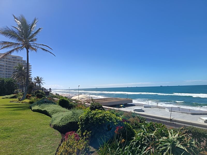A scenic elevated view of the coastline featuring a well-maintained landscaped garden and paved terrace overlooking the ocean.