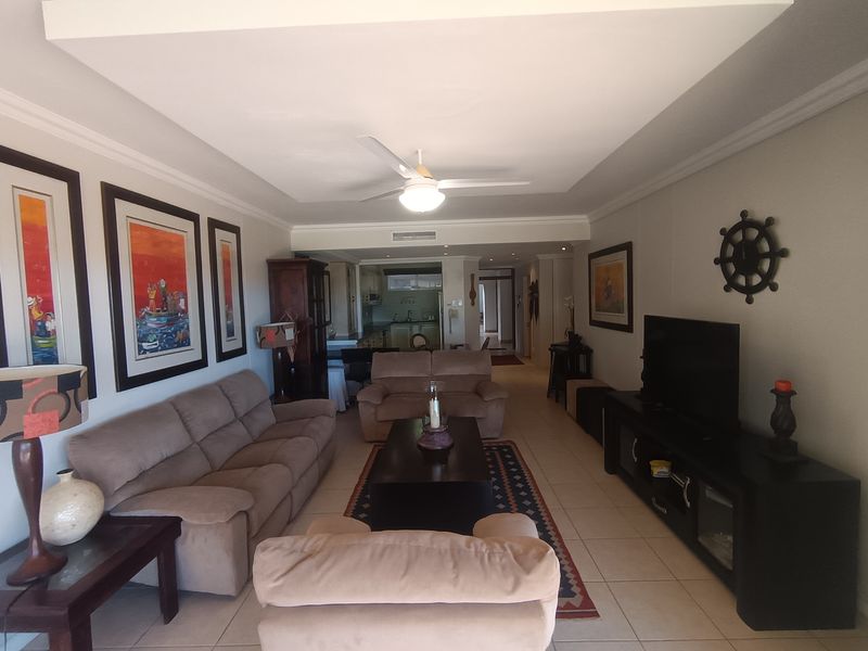 Open plan living area featuring tiled flooring, a recessed ceiling with a central fan, and a view through to the kitchen area.