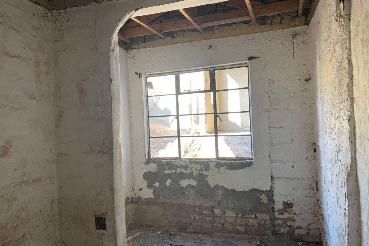 A room in shell condition featuring exposed ceiling joists, an arched doorway, and a steel-framed window, requiring significant renovation and finishing.
