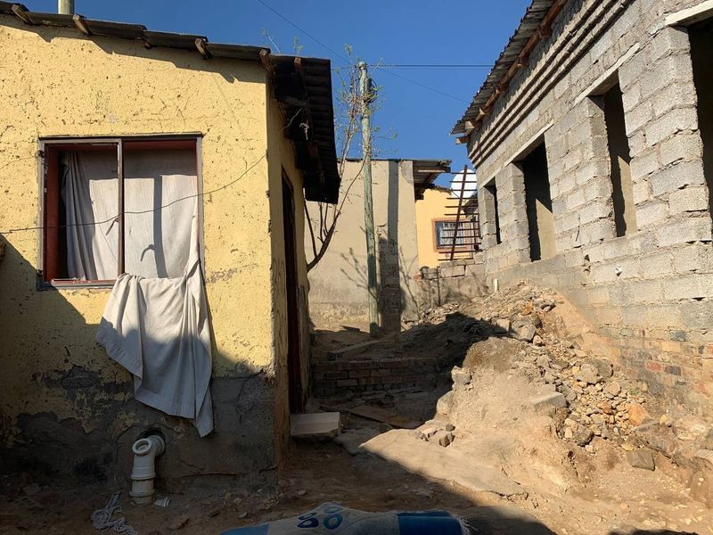 Exterior view of a property showing unfinished masonry structures, exposed brickwork, and uneven ground conditions requiring significant maintenance and completion.
