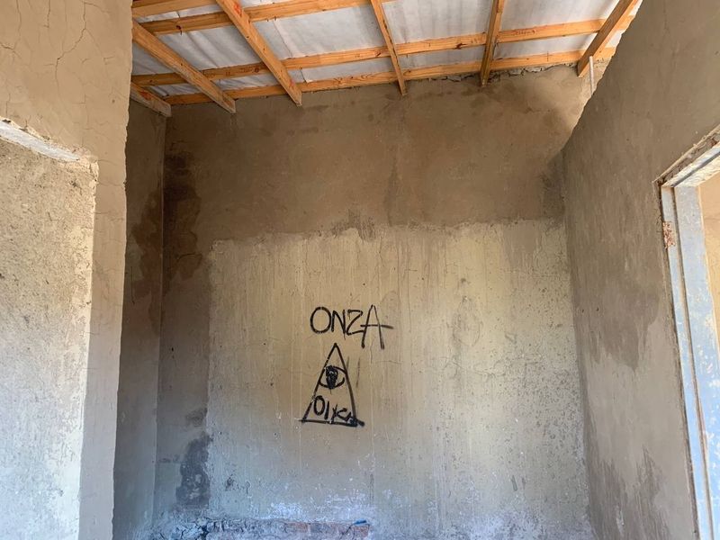 An unfinished interior space featuring exposed timber roof trusses and raw plastered masonry walls with visible graffiti and signs of damp.