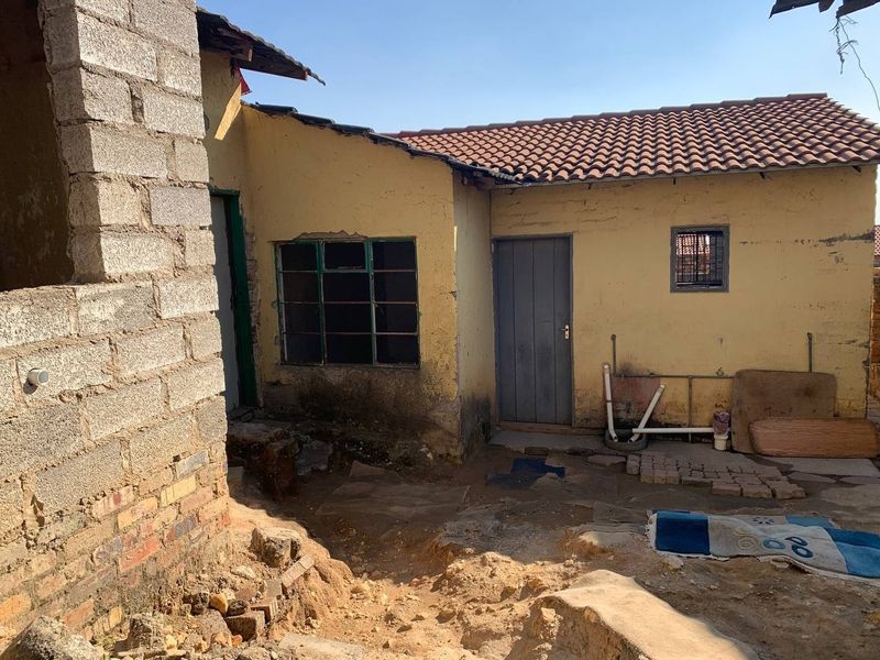 Rear exterior view of the property showing unfinished brickwork, weathered plaster walls, and basic utility access points in need of maintenance.