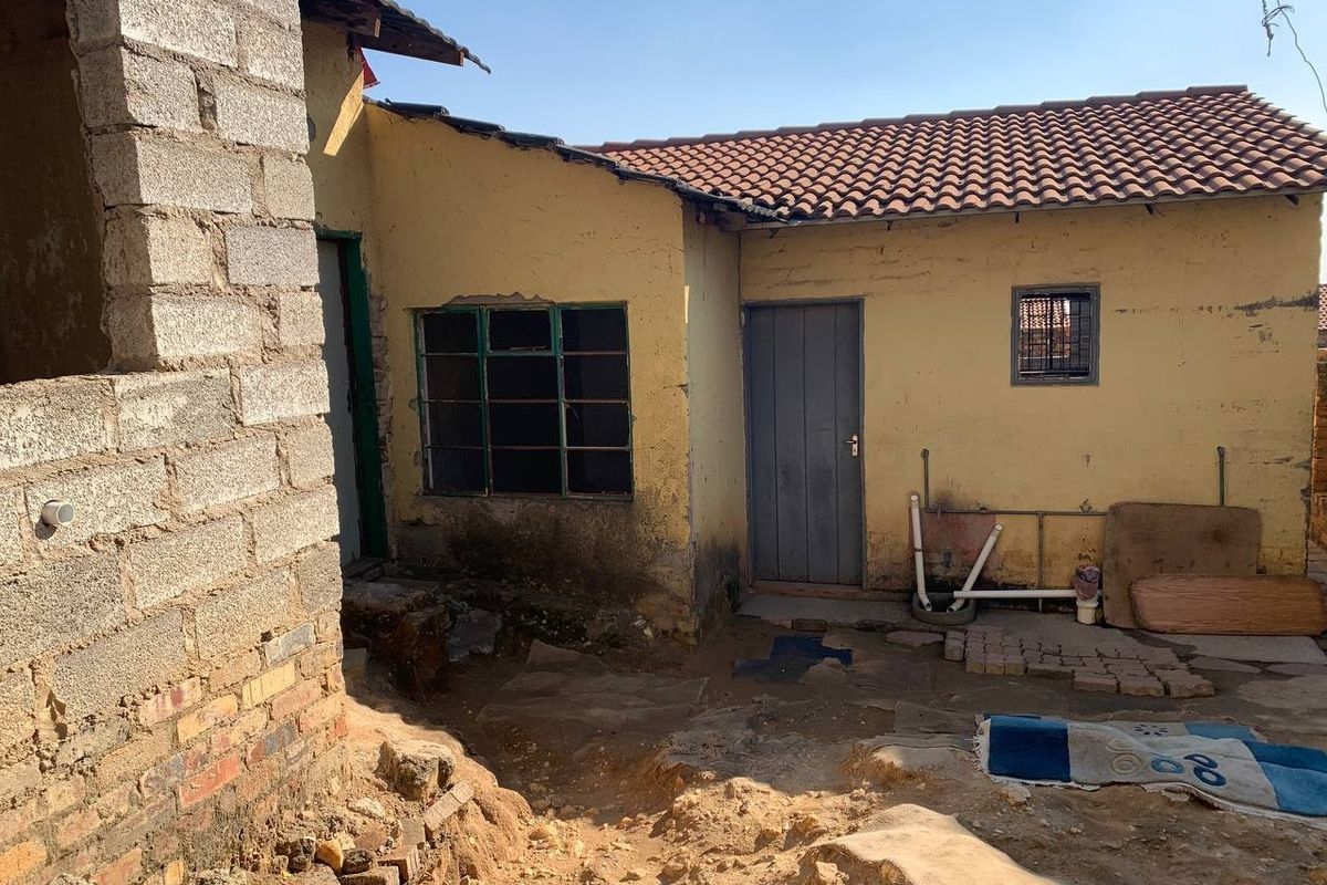 Rear exterior view of the property showing unfinished brickwork, weathered plaster walls, and basic utility access points in need of maintenance.