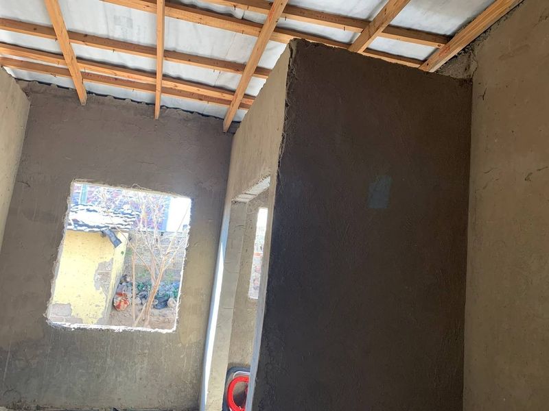 An interior view of a room under construction featuring exposed timber roof trusses and unfinished cement plastered walls.