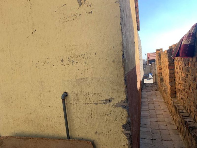 A narrow side passage featuring brick paving and a boundary wall, showing significant wear to the exterior wall plaster and paint.