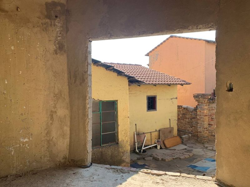 View from an unfinished interior space looking out onto a rear courtyard with weathered outbuildings and exposed brick structures.