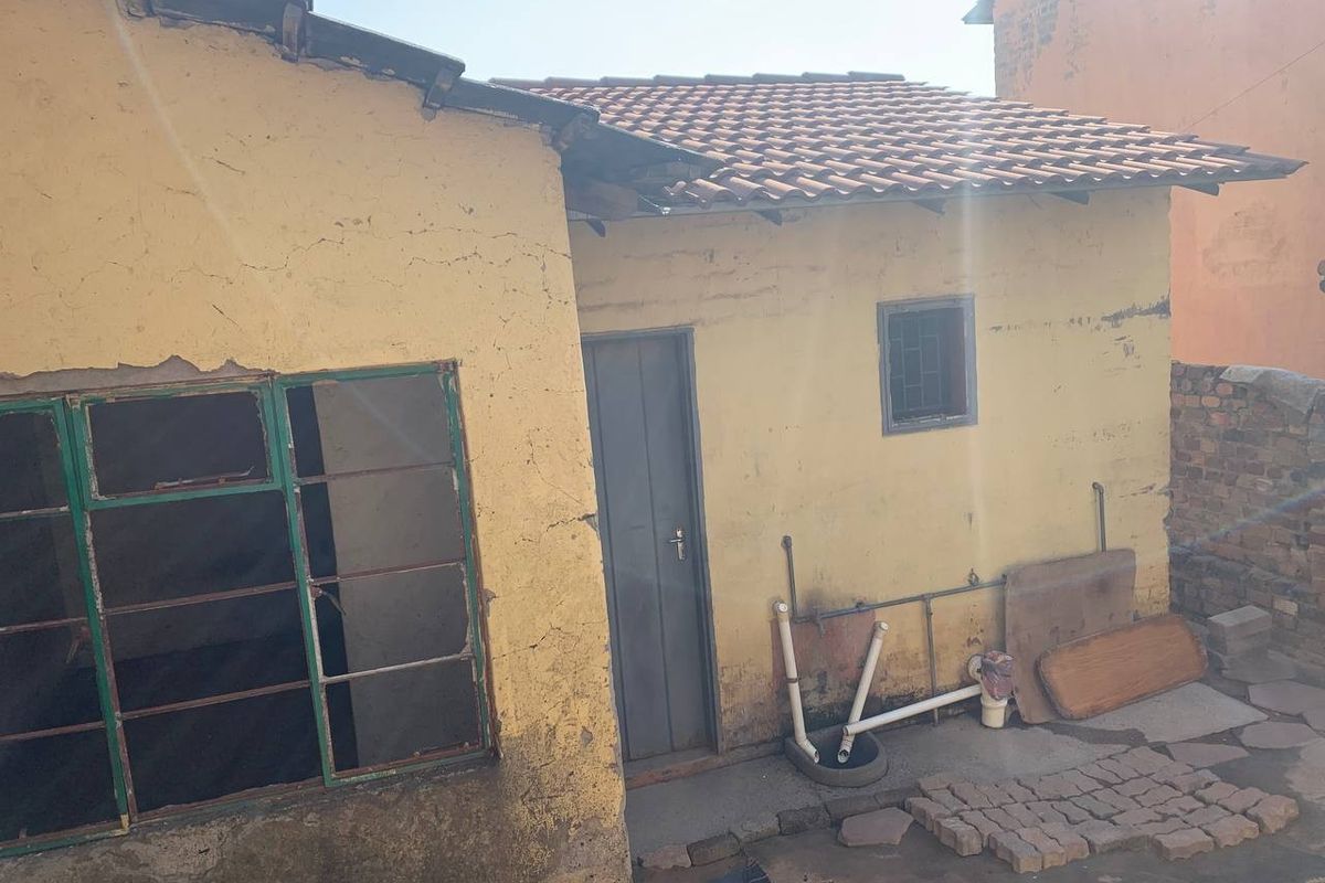 Rear exterior view of a house showing weathered yellow plaster walls, tiled roofing, and exposed external plumbing fixtures.