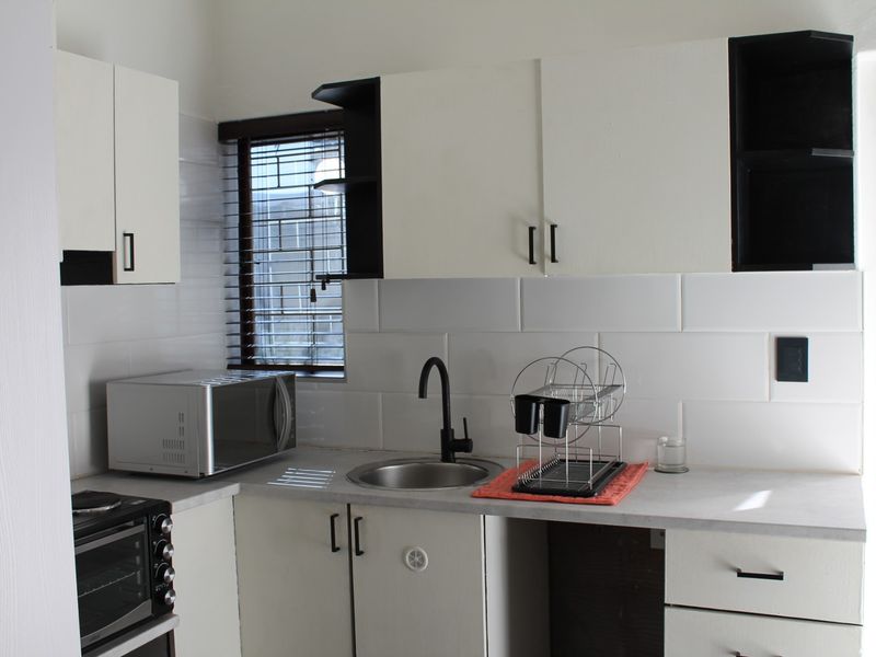A compact, functional kitchen featuring white cabinetry, a modern black tap, stainless steel sink, and tiled backsplash with direct access to the outdoors.
