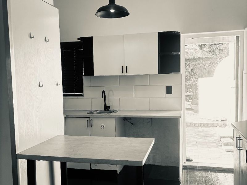 A compact kitchen featuring white cabinetry, a subway tile backsplash, and dark timber flooring, with direct access to an outdoor area.