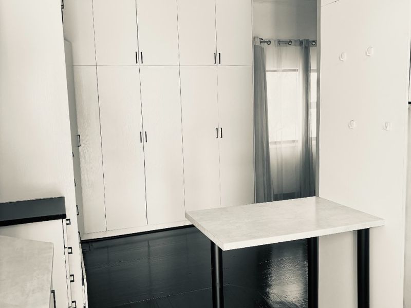 A clean, minimalist kitchen area featuring white built-in cabinetry, dark hardwood flooring, and a functional breakfast bar setup.