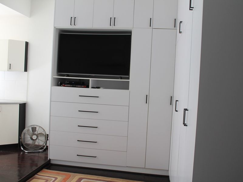 A living area featuring extensive modern white built-in cabinetry and integrated storage units with dark hardware.