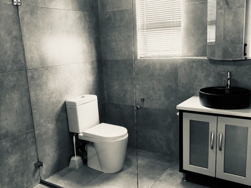 Modern bathroom featuring large-format grey wall and floor tiles, a walk-in glass shower, a vanity with a vessel sink, and a toilet.