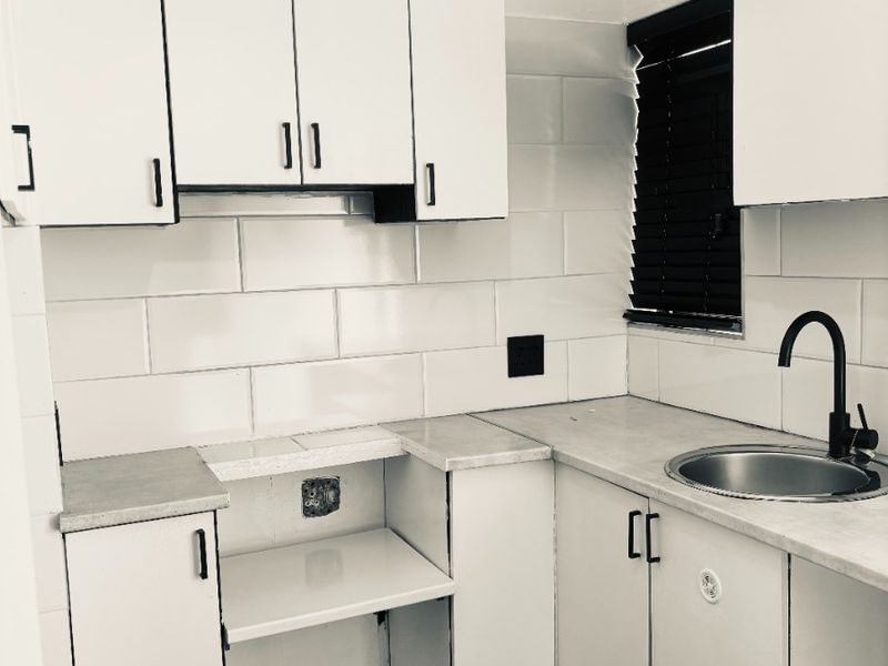 A compact kitchen featuring white cabinetry, subway tile backsplash, stainless steel sink with black tap, and laminate countertops.