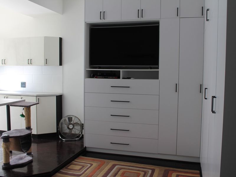 Open plan living area featuring extensive built-in white cabinetry, integrated storage, and a functional kitchen counter with tiled backsplash.