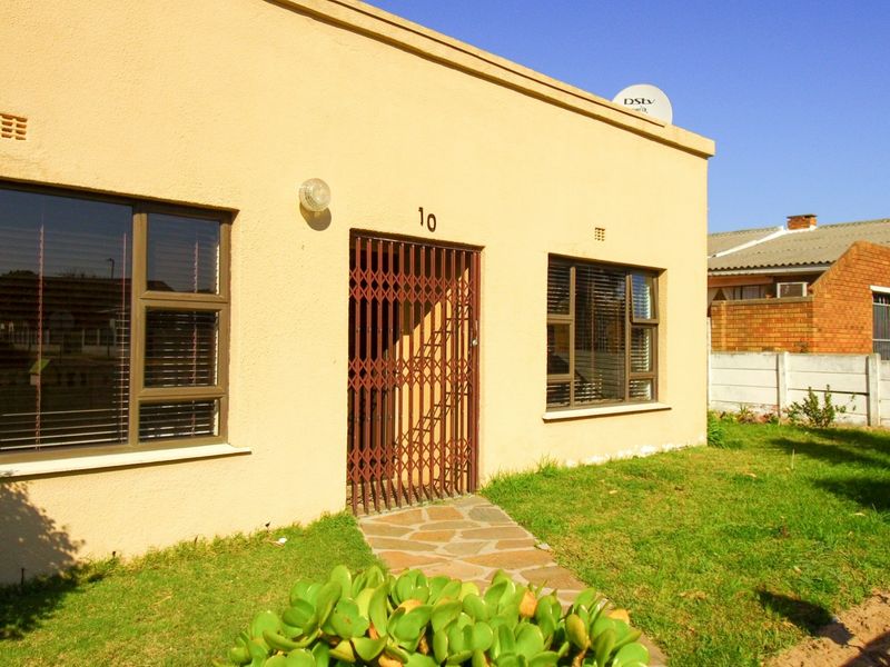 Front facade of a single-story house featuring plastered walls, aluminium window frames, a security gate entrance, and a stone paved walkway.