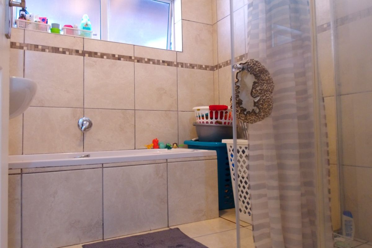 A functional bathroom featuring a built-in bathtub, separate shower enclosure, and neutral wall and floor tiling.