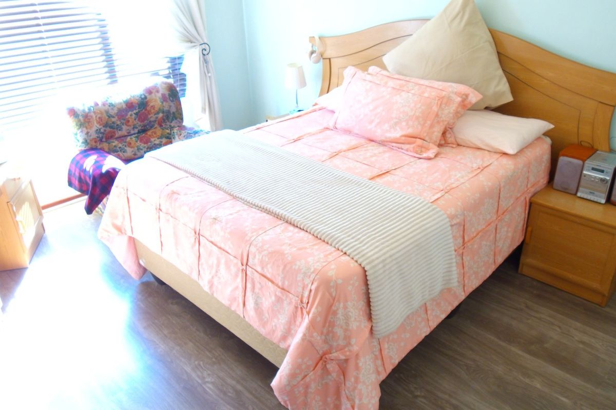 A bedroom featuring laminate flooring and venetian blinds, offering a functional space with natural light.
