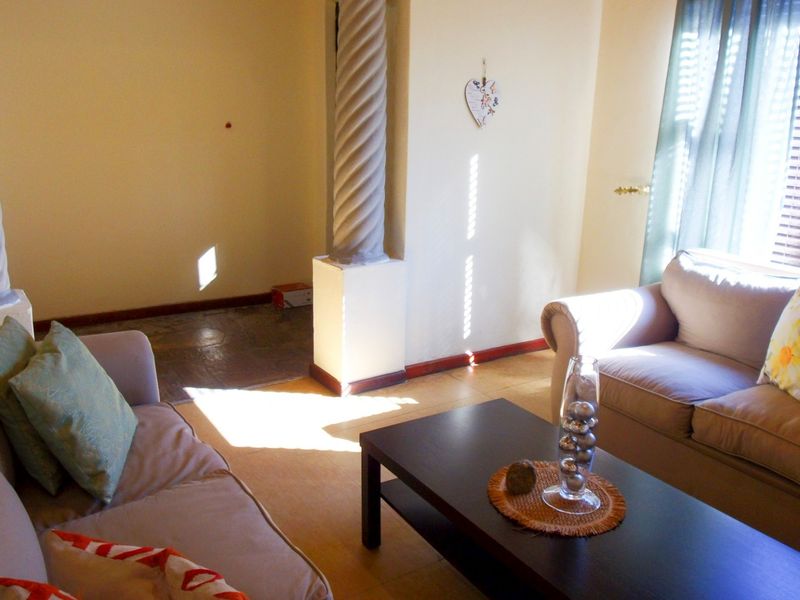 A living room featuring decorative columns, tiled flooring, and venetian blinds, offering a functional space with natural light.