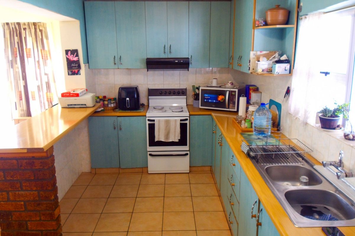 A functional kitchen featuring dated blue cabinetry, laminate countertops, a double stainless steel sink, and a freestanding stove with an extractor fan.