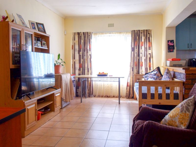 Open-plan living area featuring tiled flooring and a connected kitchen space with a brick breakfast bar and ample natural light.