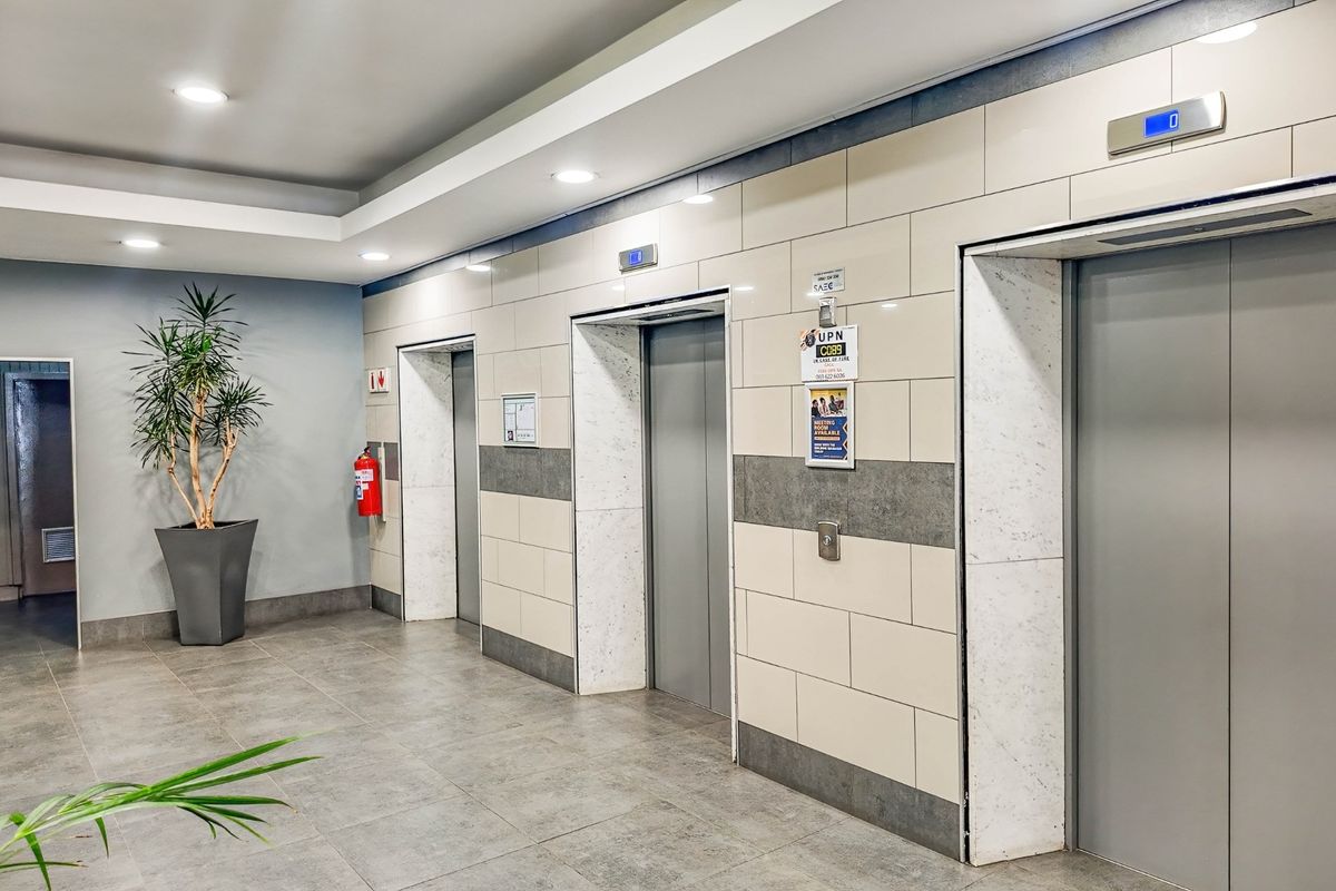 Modern commercial building elevator lobby featuring tiled walls, grey floor tiles, and recessed ceiling lighting.
