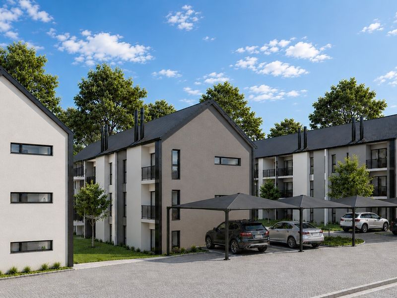 Modern apartment complex featuring multi-story residential buildings with balconies, covered parking bays, and a paved driveway.