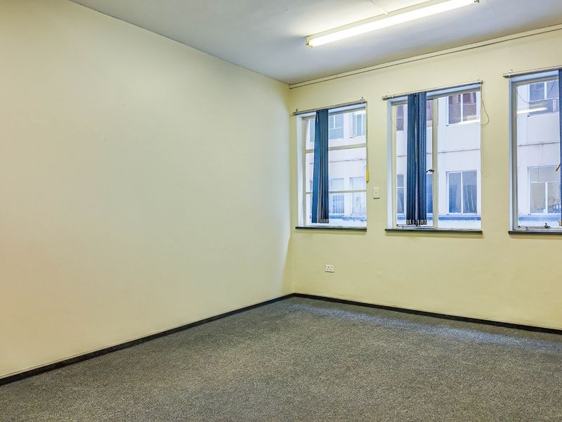 An empty, functional office space featuring neutral walls, carpeted flooring, and large windows providing natural light.