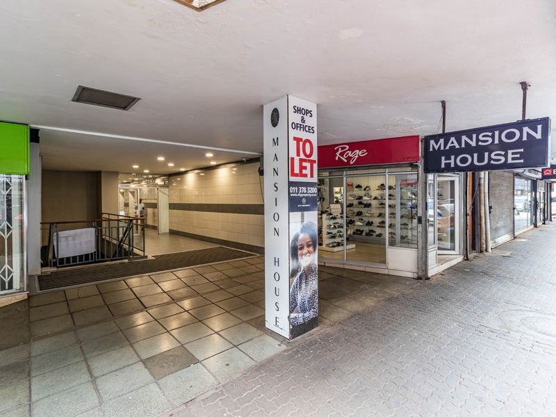 Street-level view of the Mansion House commercial building entrance, featuring retail storefronts, a covered walkway, and access to upper-level office spaces.