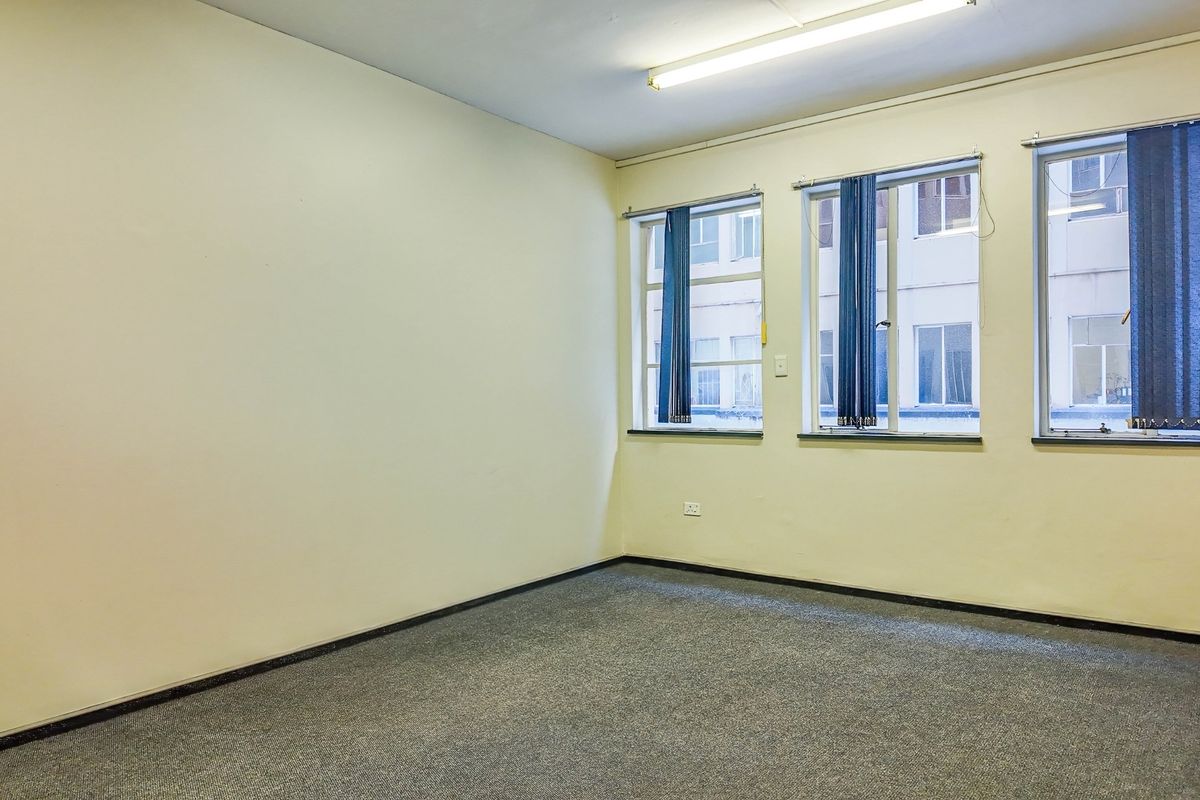 An empty, functional office space featuring neutral walls, carpeted flooring, and large windows providing natural light.