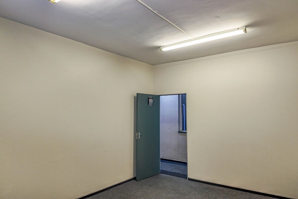 A vacant, neutral-toned office space featuring carpeted flooring and overhead fluorescent lighting, providing a clean and functional commercial work environment.
