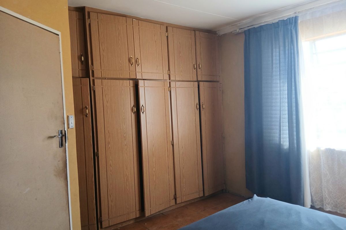 A bedroom featuring extensive built-in wooden cupboards and tiled flooring, offering ample storage space with potential for cosmetic updates.