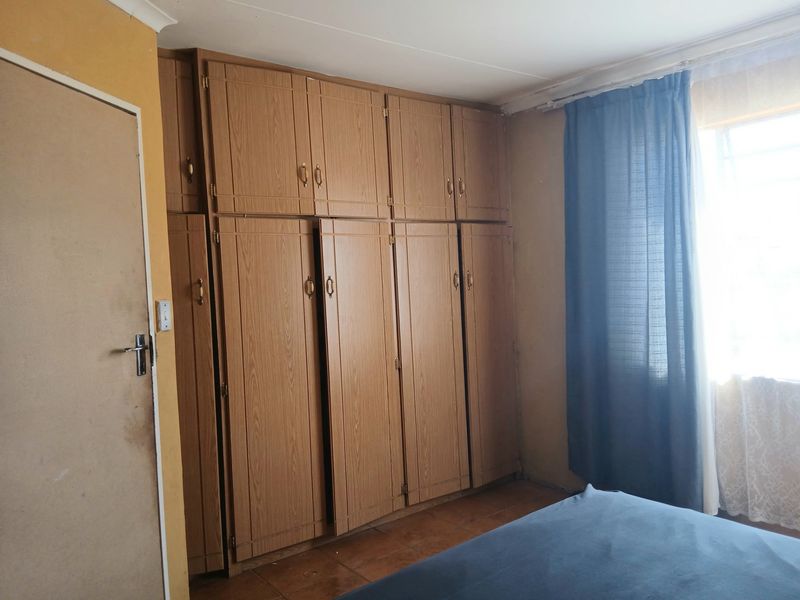 A bedroom featuring extensive built-in wooden cupboards and tiled flooring, offering ample storage space with potential for cosmetic updates.