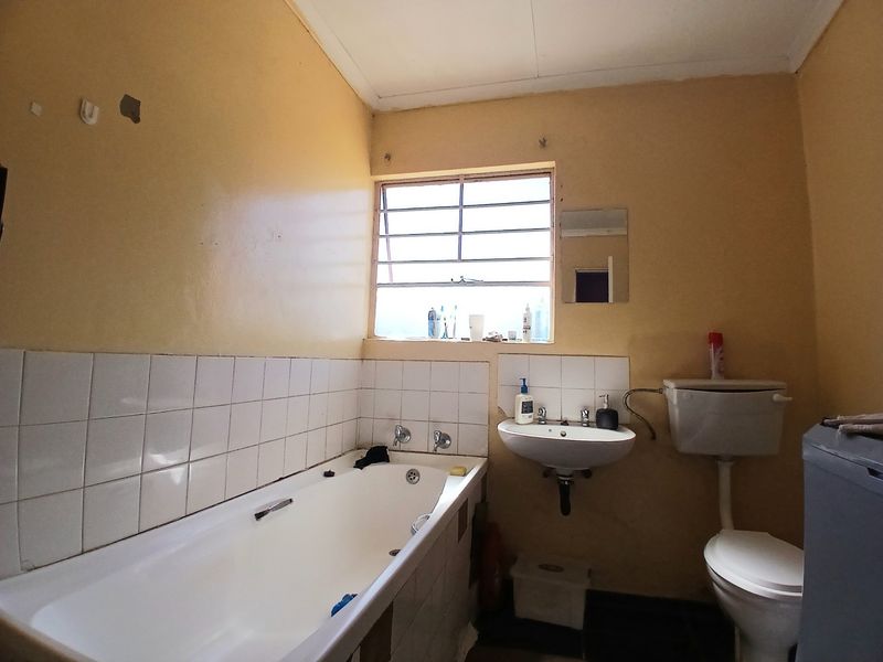 A dated bathroom featuring a standard bathtub, wall-mounted basin, and toilet, requiring cosmetic updates and wall repairs to modernize the space.