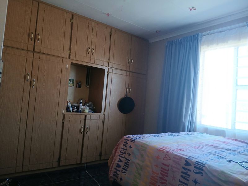 A bedroom featuring extensive built-in wooden cabinetry, tiled flooring, and a window with security bars, offering functional storage space.