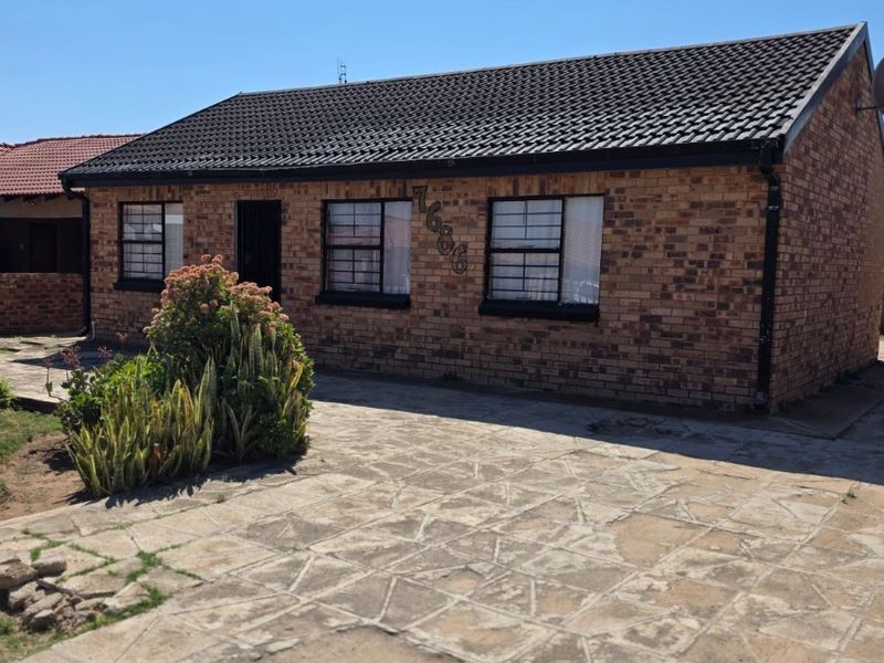 A single-story face brick house featuring a tiled roof, security bars on windows, and a paved driveway area.