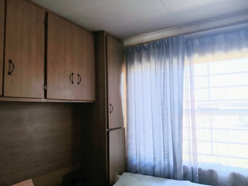 A bedroom featuring built-in wooden cupboards and a window fitted with security bars, offering a functional space ready for updates.