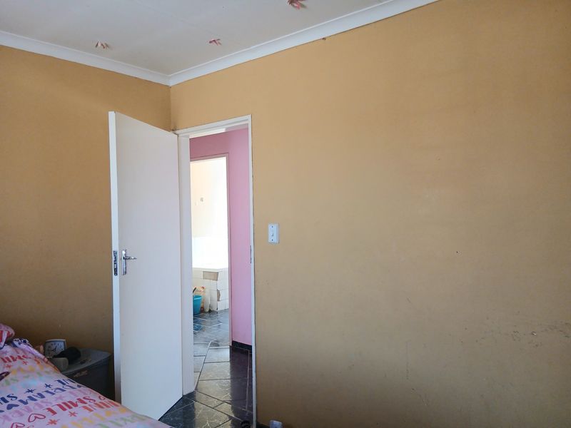 A bedroom interior featuring plain walls with visible scuff marks and a doorway leading to an adjacent tiled bathroom area.